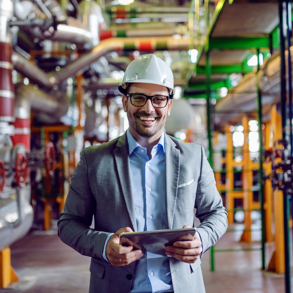 Man standing in warehouse in a hard hat holding an ipad